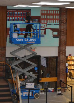 Iris Menegay ont eh lift painting a mural above the front door