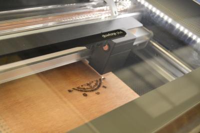 The Glowforge laser engraves an image on wood.